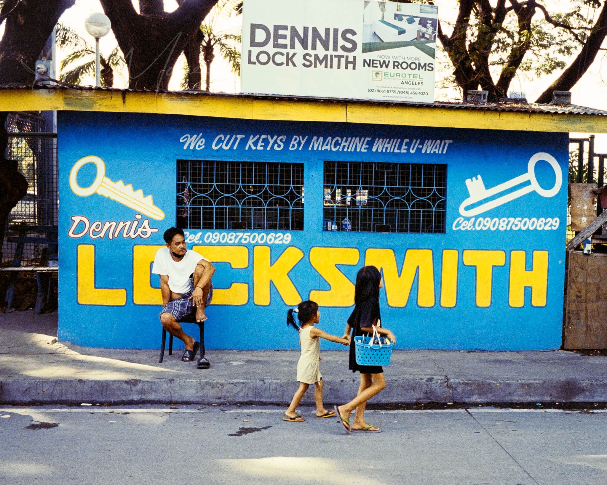 Vibrant street scene with people outside a blue Philippine locksmith shop on a sunny day.