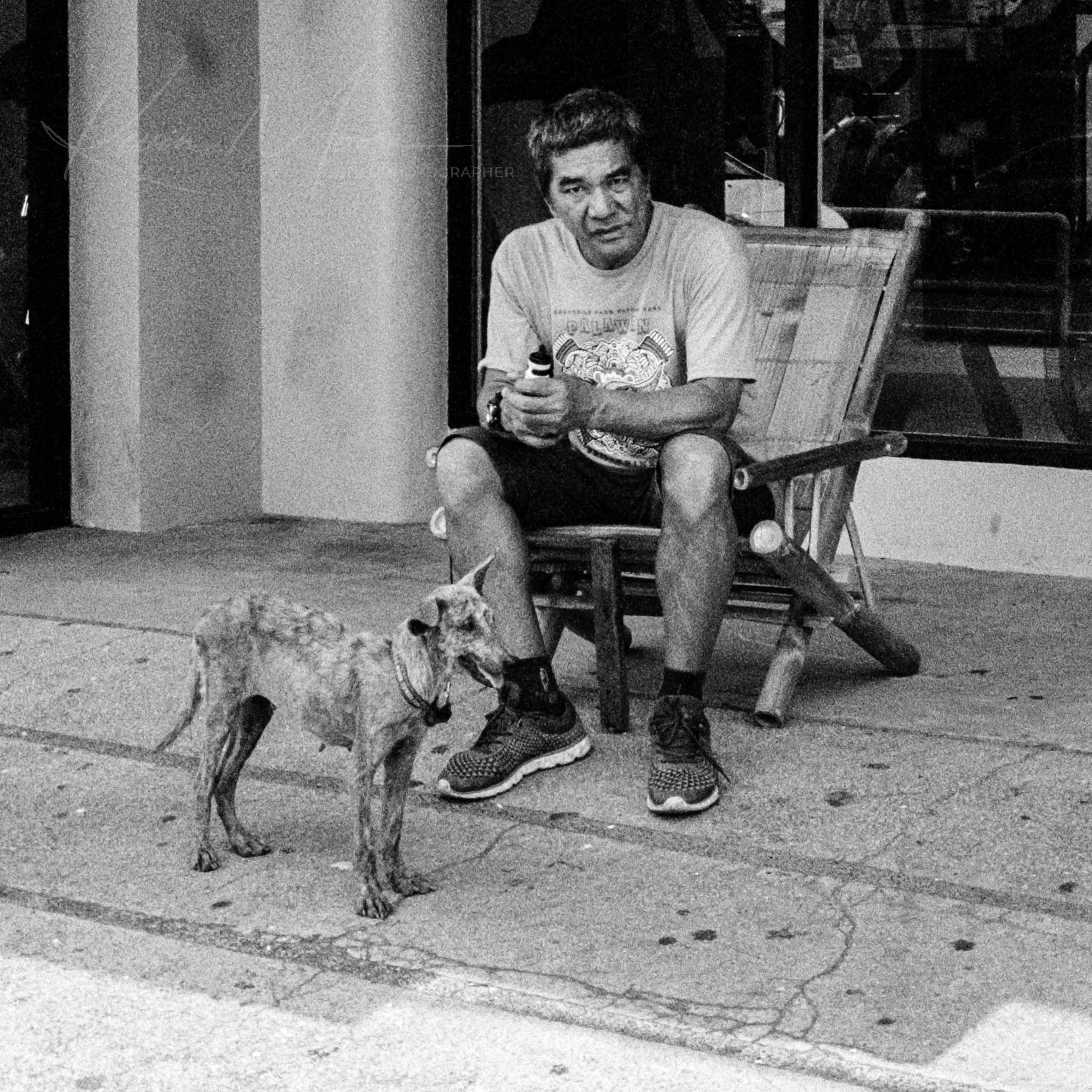 Man peacefully enjoying urban solitude with attentive terrier mix dog on city sidewalk in black and white.