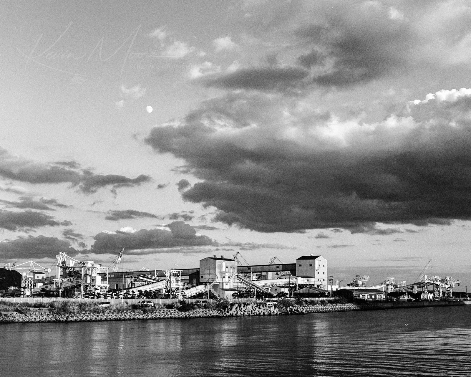 Monochrome photo of moonrise over tranquil city waterfront reflecting urban architecture.