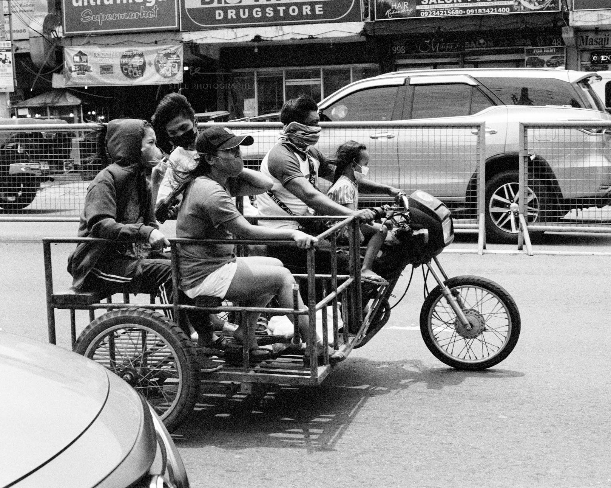Multi-passenger motorcycle sidecar on busy city street, black and white photo.