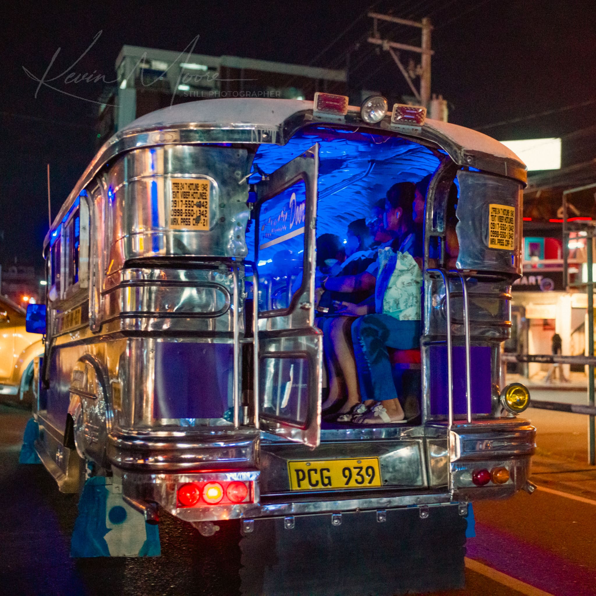 Passengers enjoying a night ride in a lit-up, silver jeepney in the busy streets of Philippines.