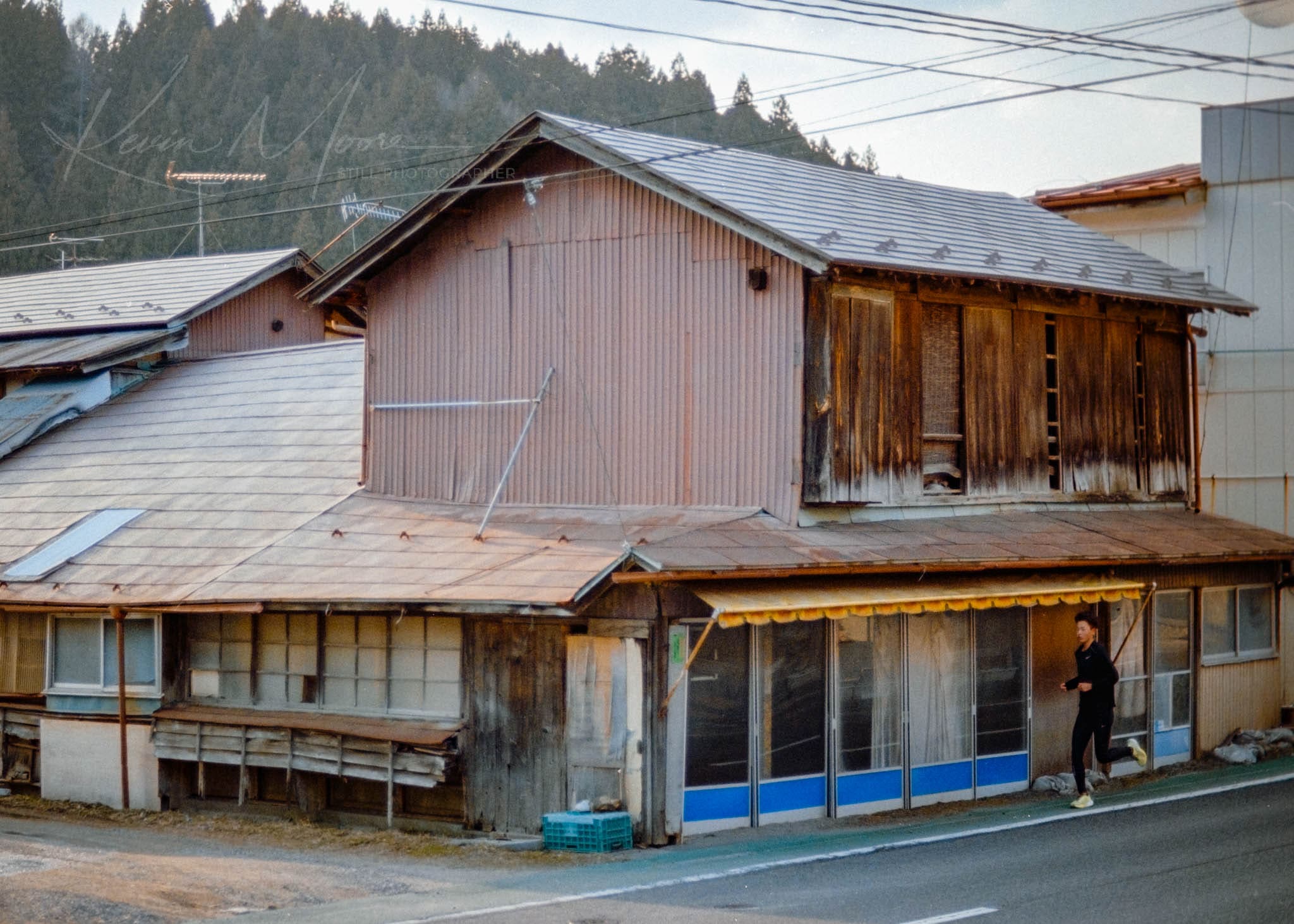 Lonely figure passing weathered building in serene, rural setting at dusk