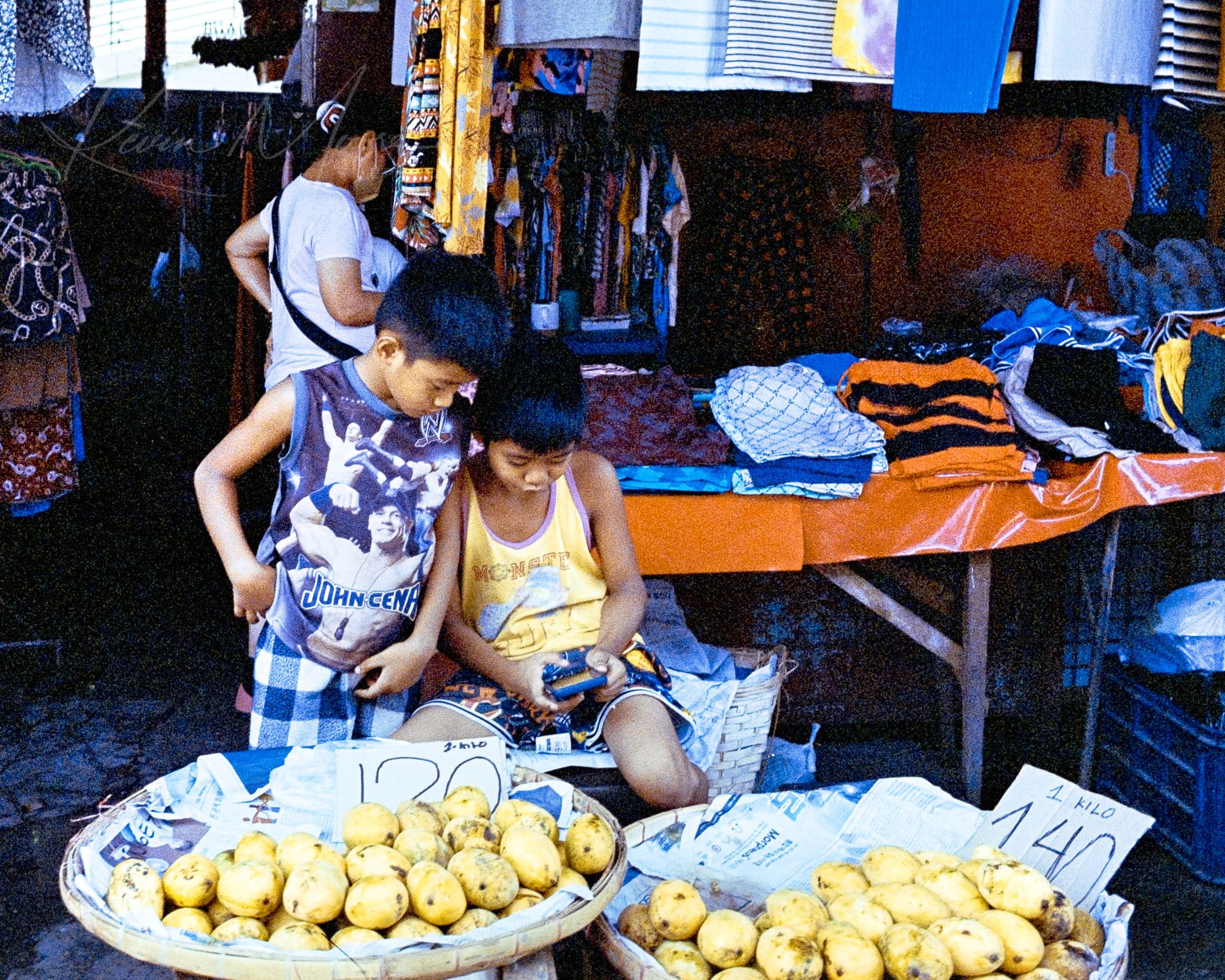 Children selling mangoes at a bustling, colorful outdoor market during daytime.