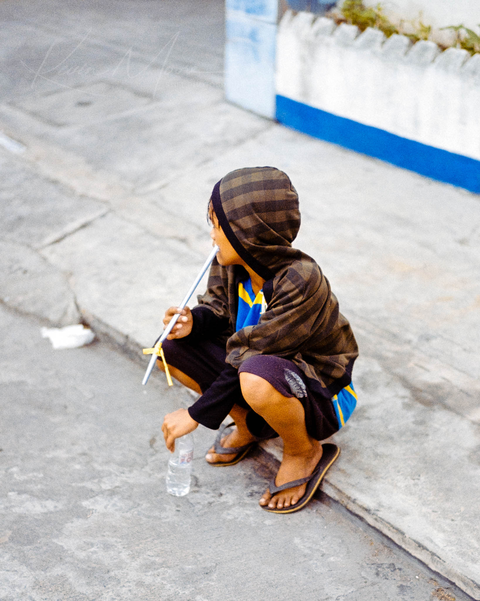 Individual in colorful attire sipping drink on urban sidewalk in thoughtful solitude.