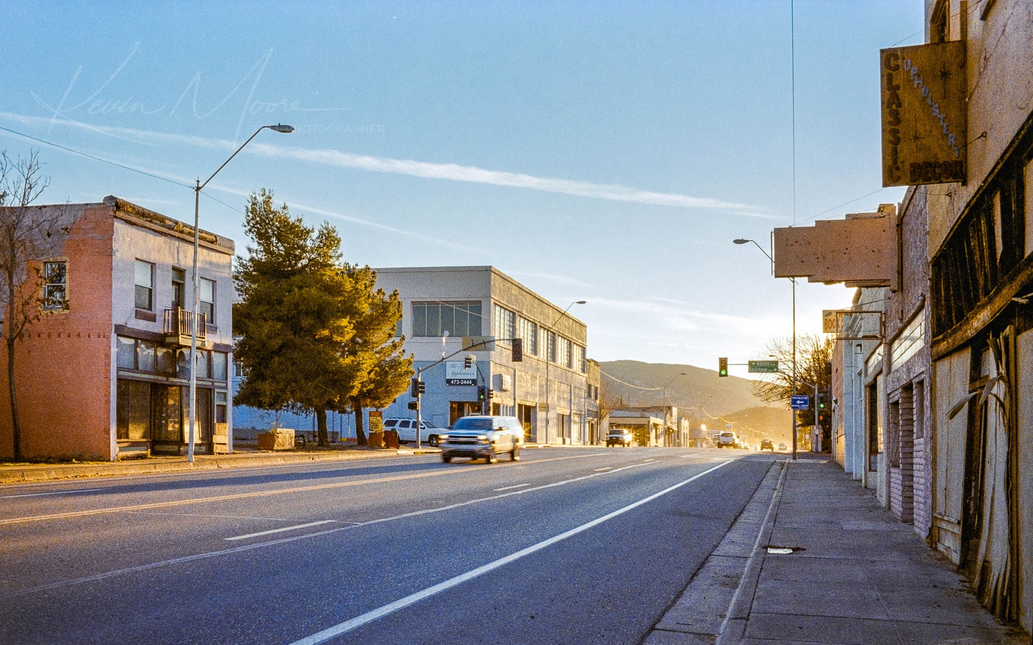 Peaceful small-town street at dawn with diverse architecture and minimal traffic.