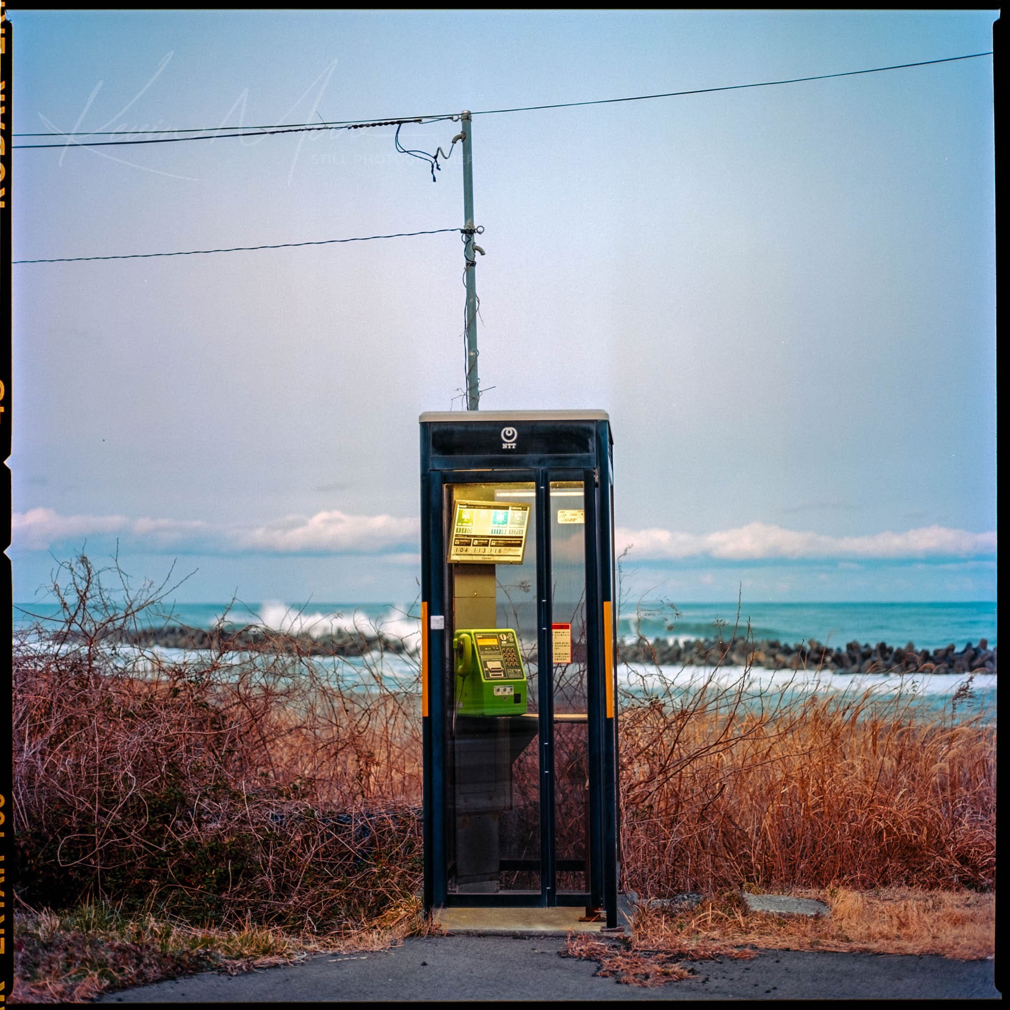 Vintage phone booth in tranquil wilderness with distant hills and power lines overhead.