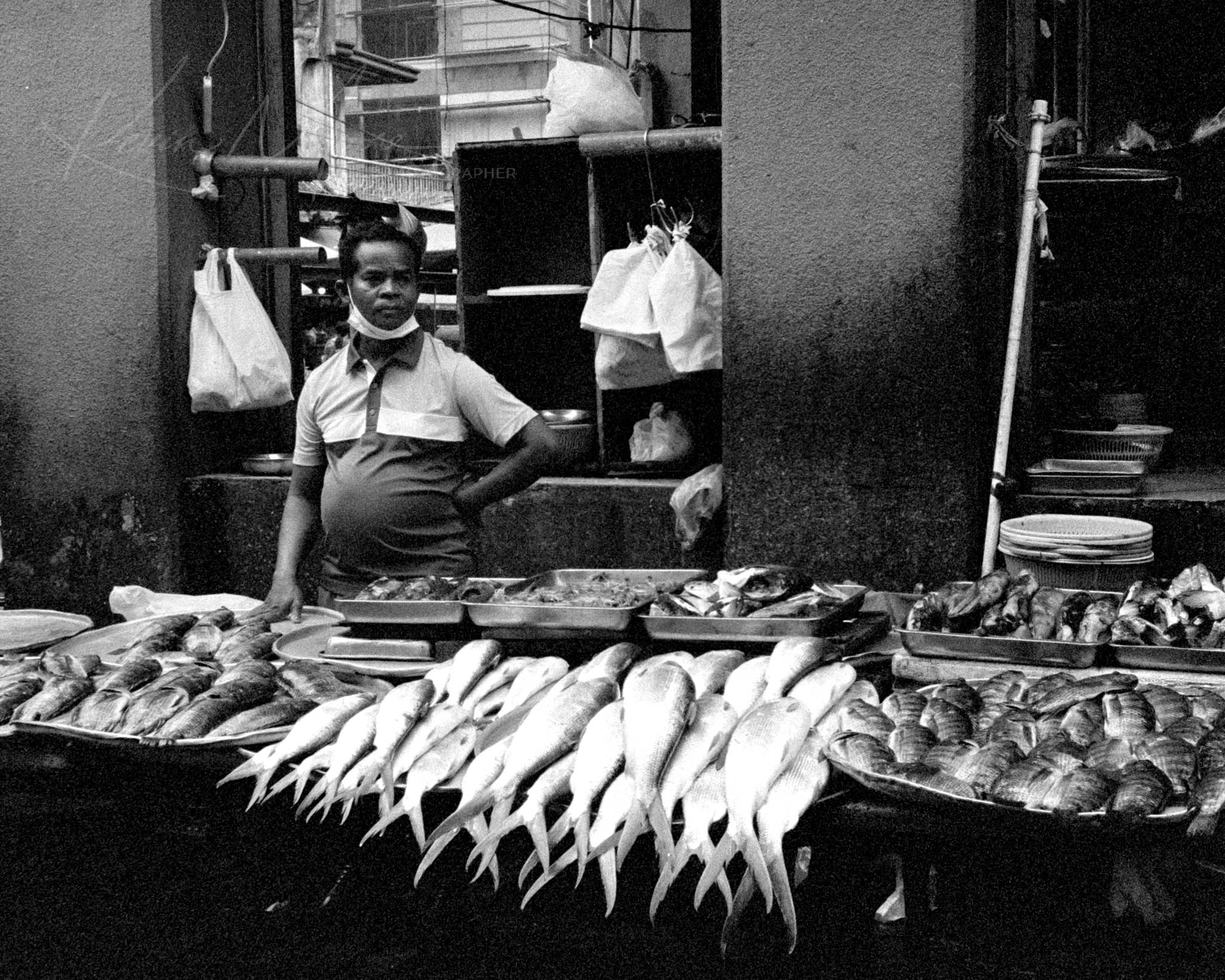 Smiling woman selling assorted fish at a traditional market in black-and-white photo.