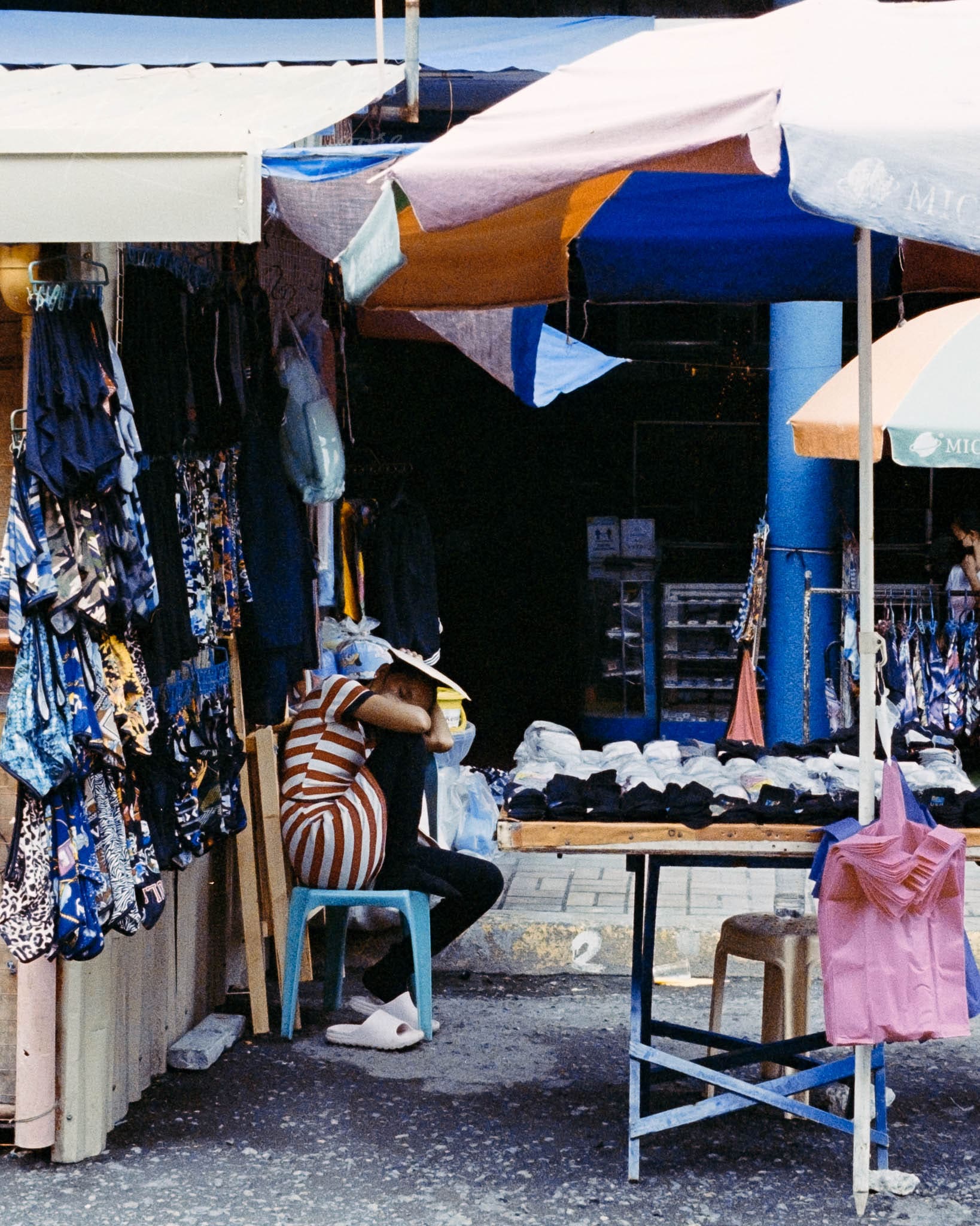 Vibrant clothing stalls at open-air market with solitary figure examining merchandise.