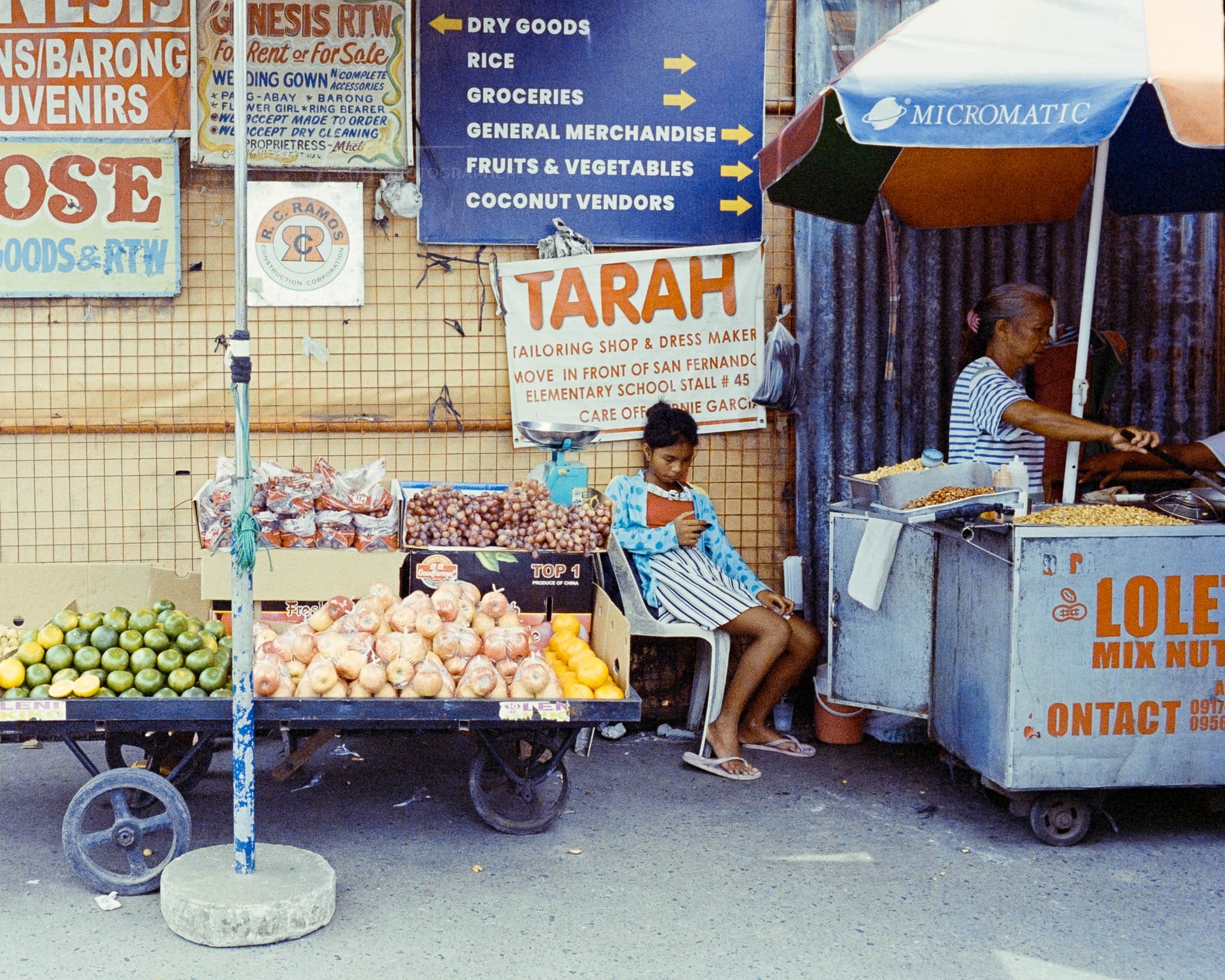 Girl and vendor in a lively street market with a colorful, mobile fruit cart.