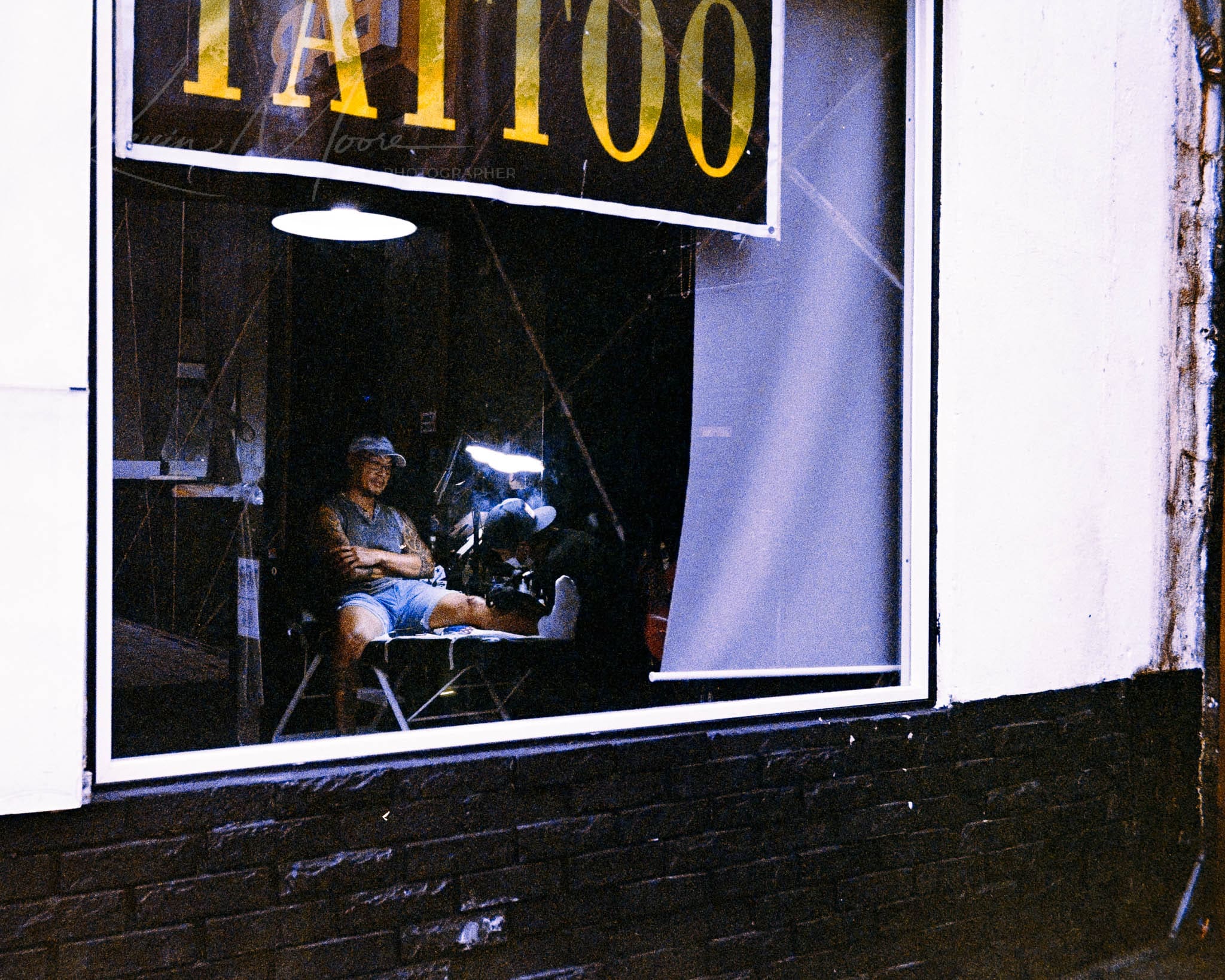 Individual in a dim-lit tattoo parlor reflecting on art, contrasted with bustling city life.