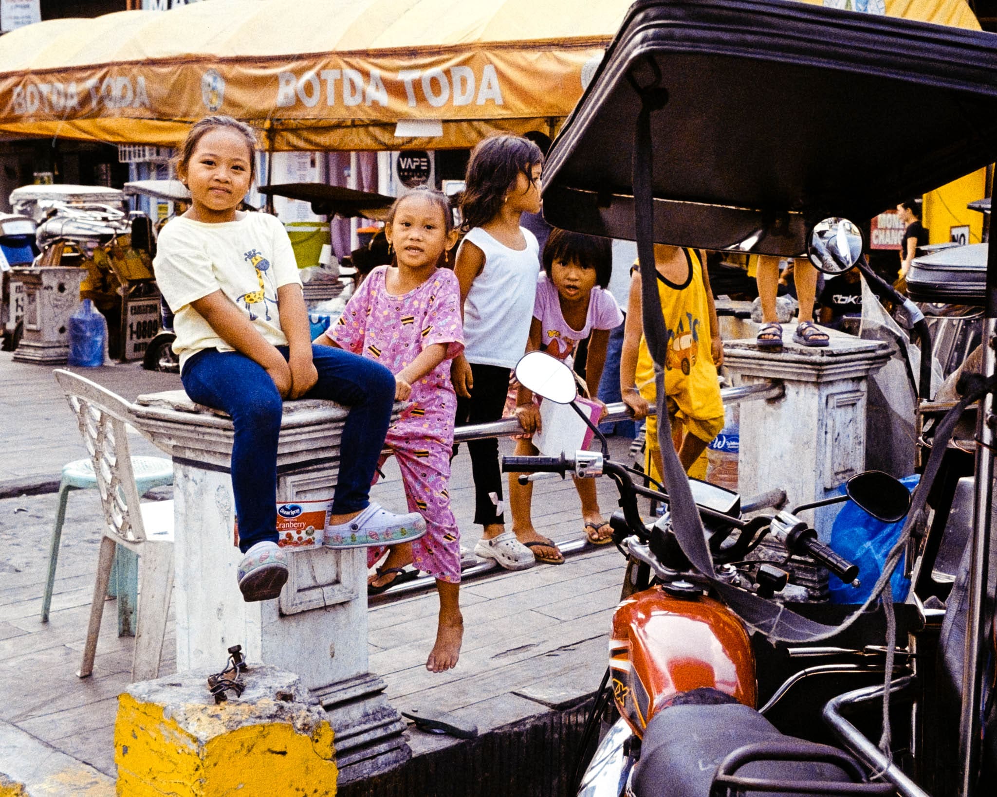 Three girls exploring local city market amidst colorful canopy and motorcycles