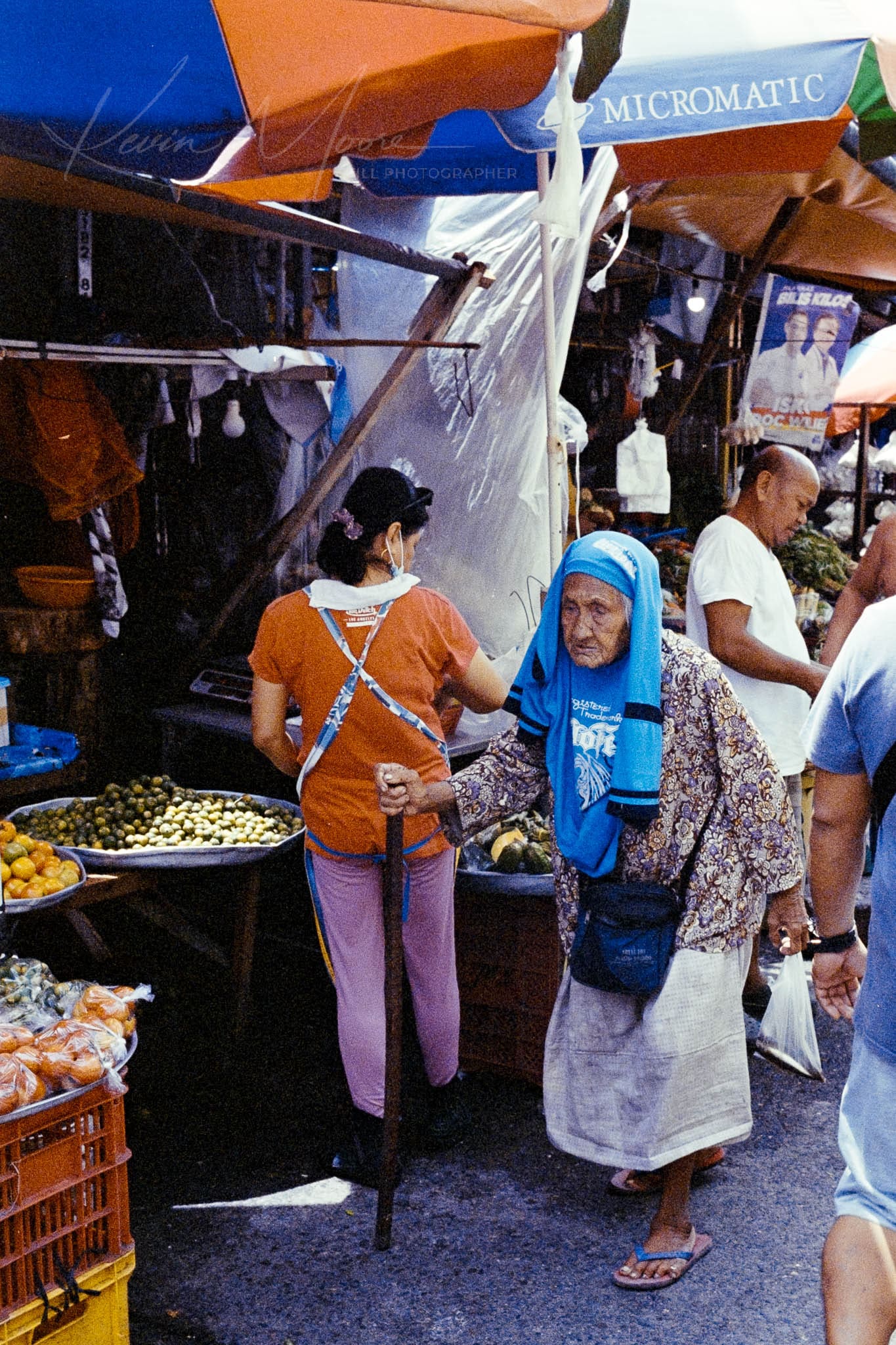 Elderly woman in traditional dress shopping at lively, diverse food market.
