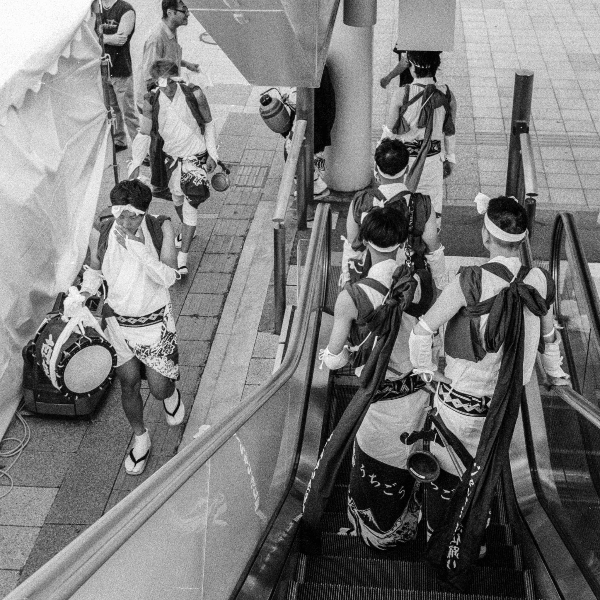 Japanese drummers in traditional attire on escalator, merging culture with modern urban life.