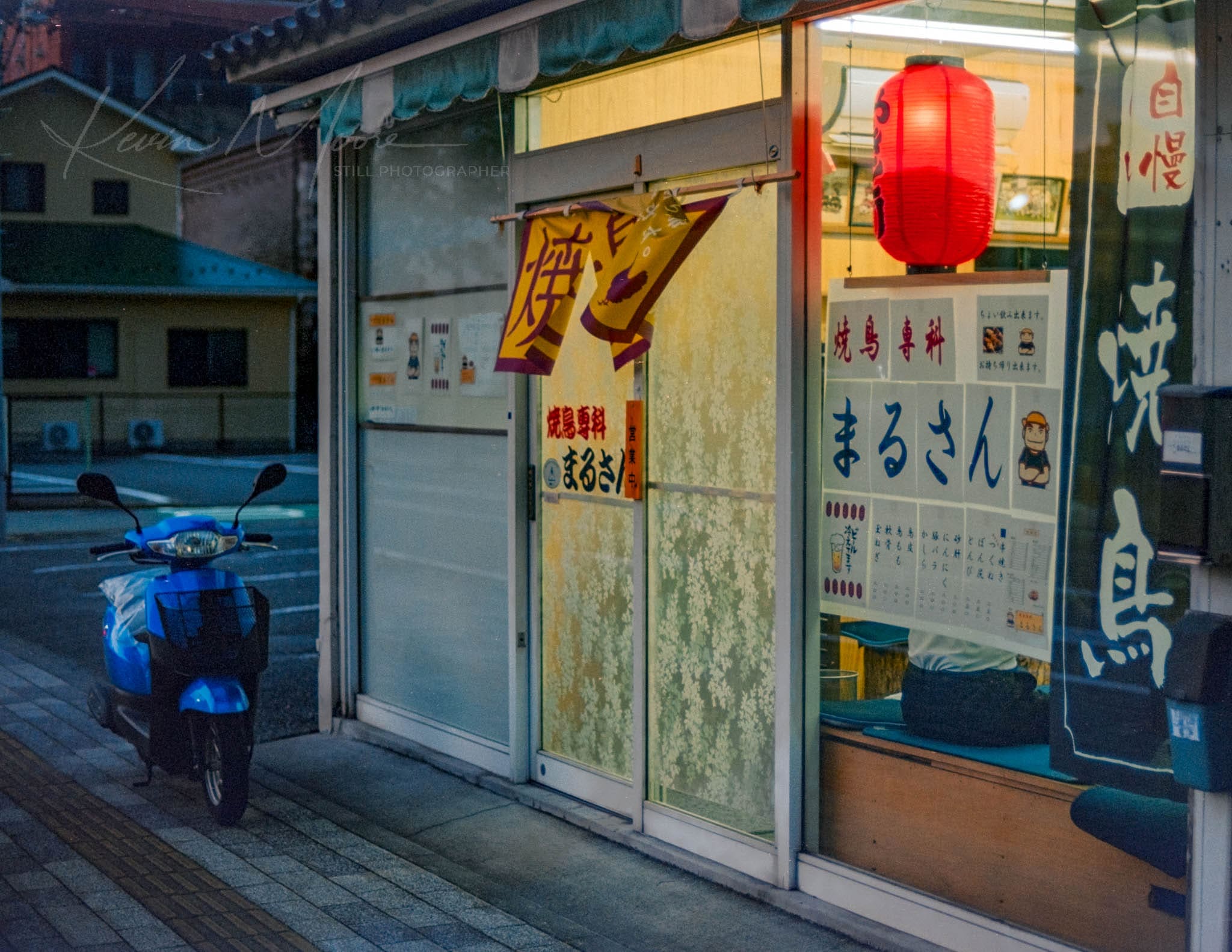 Traditional Japanese restaurant at dusk, marked by a glowing red lantern and parked motorbike.