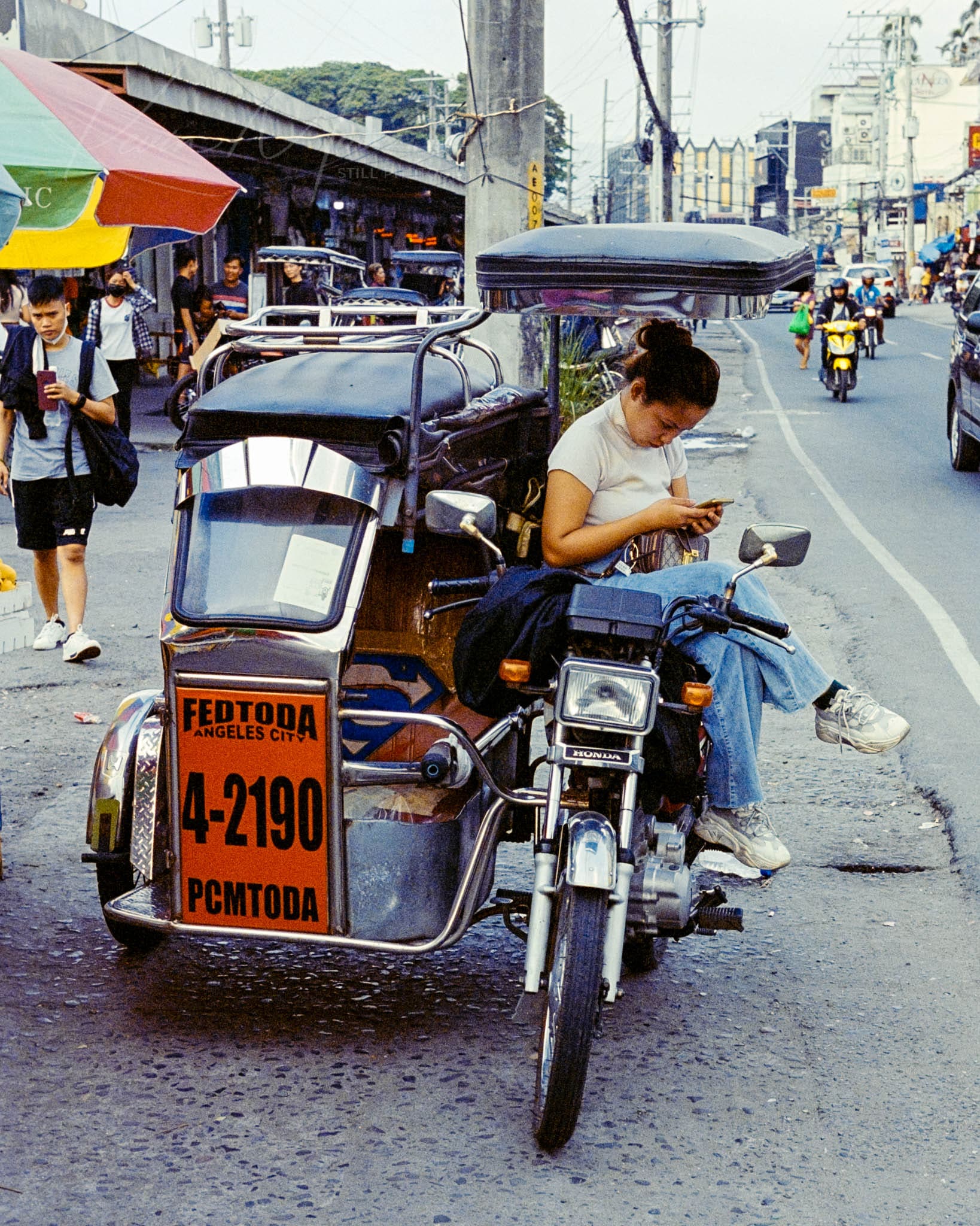 Tricycle taxi driver engrossed in mobile amidst bustling urban city life.