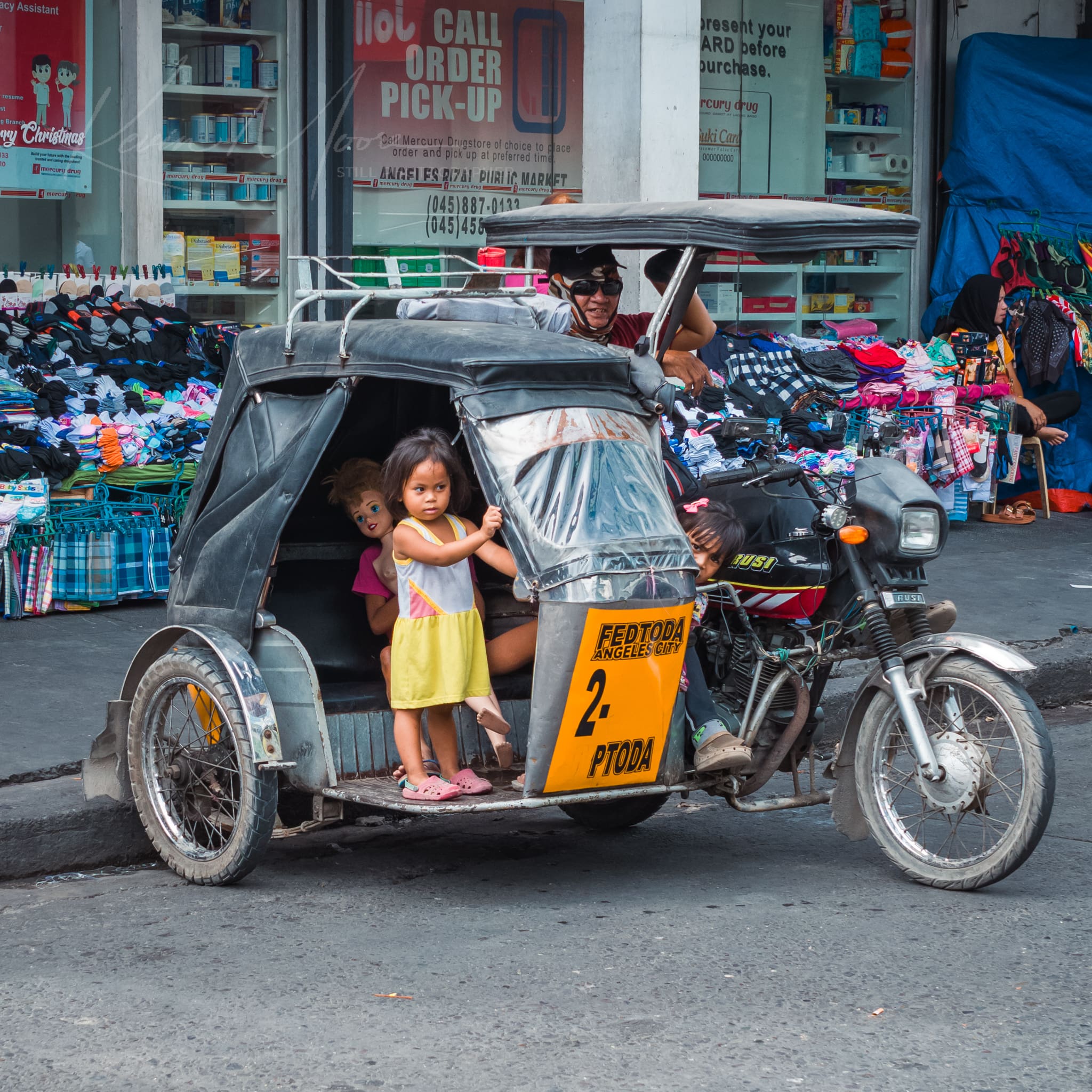 Motorized tricycle with children and driver in urban Philippines marketplace.
