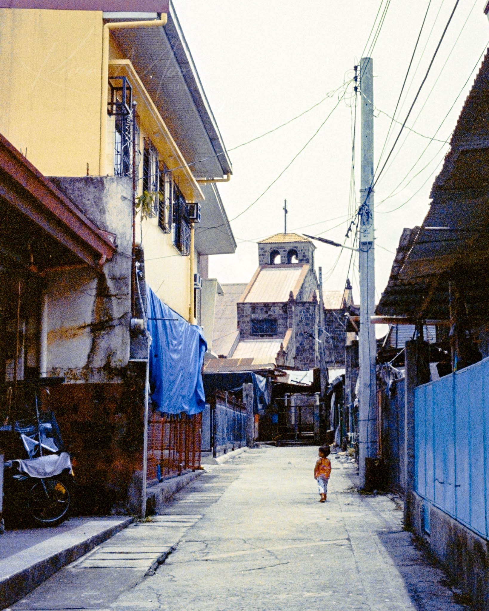 Child walking on vibrant, tropical street with colorful residential buildings and urban utilities.