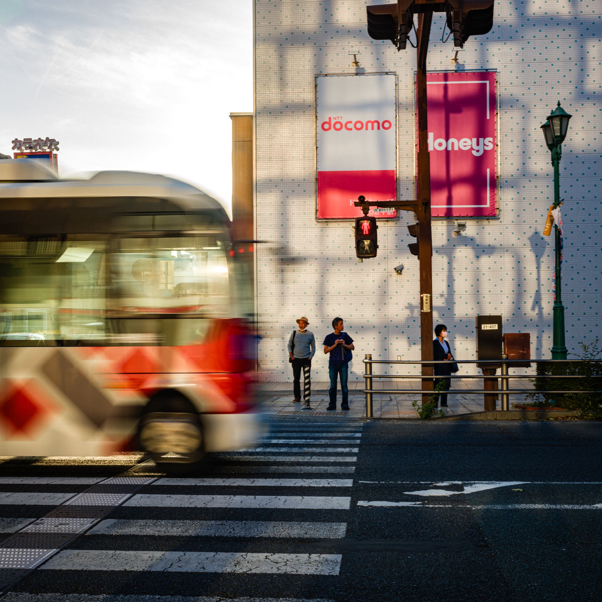 Fast-moving bus and pedestrians at a crosswalk during golden hour in a Japanese city.