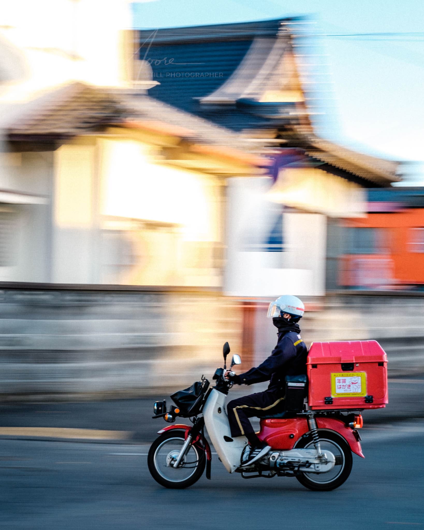 Postal driver on motorcycle speeding through Iwaki City Japan during golden hour.