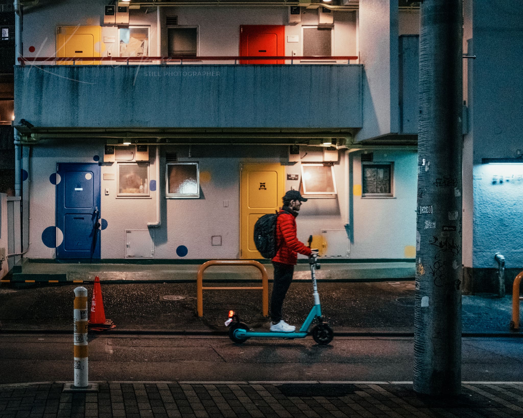 Person in red jacket contemplating next move by colorful urban building at night.