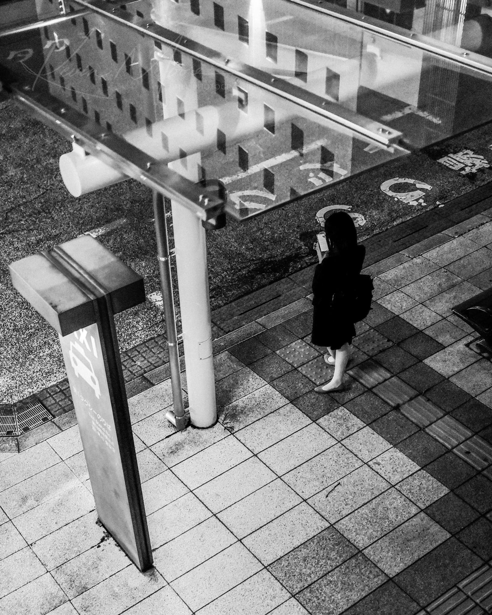 Solitary figure on tiled pavement under Japanese signboard at night.
