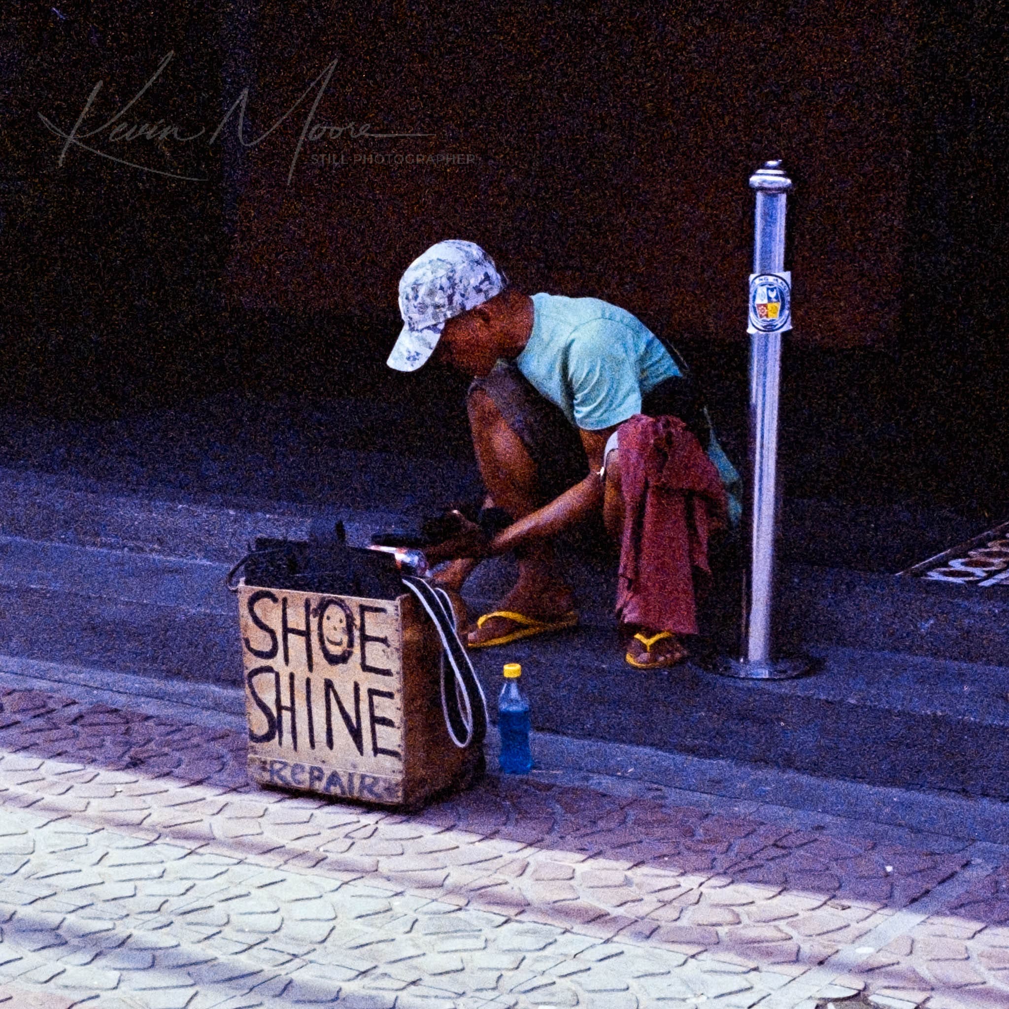 Street shoe shiner in casual attire preparing for work in a summery urban setting.