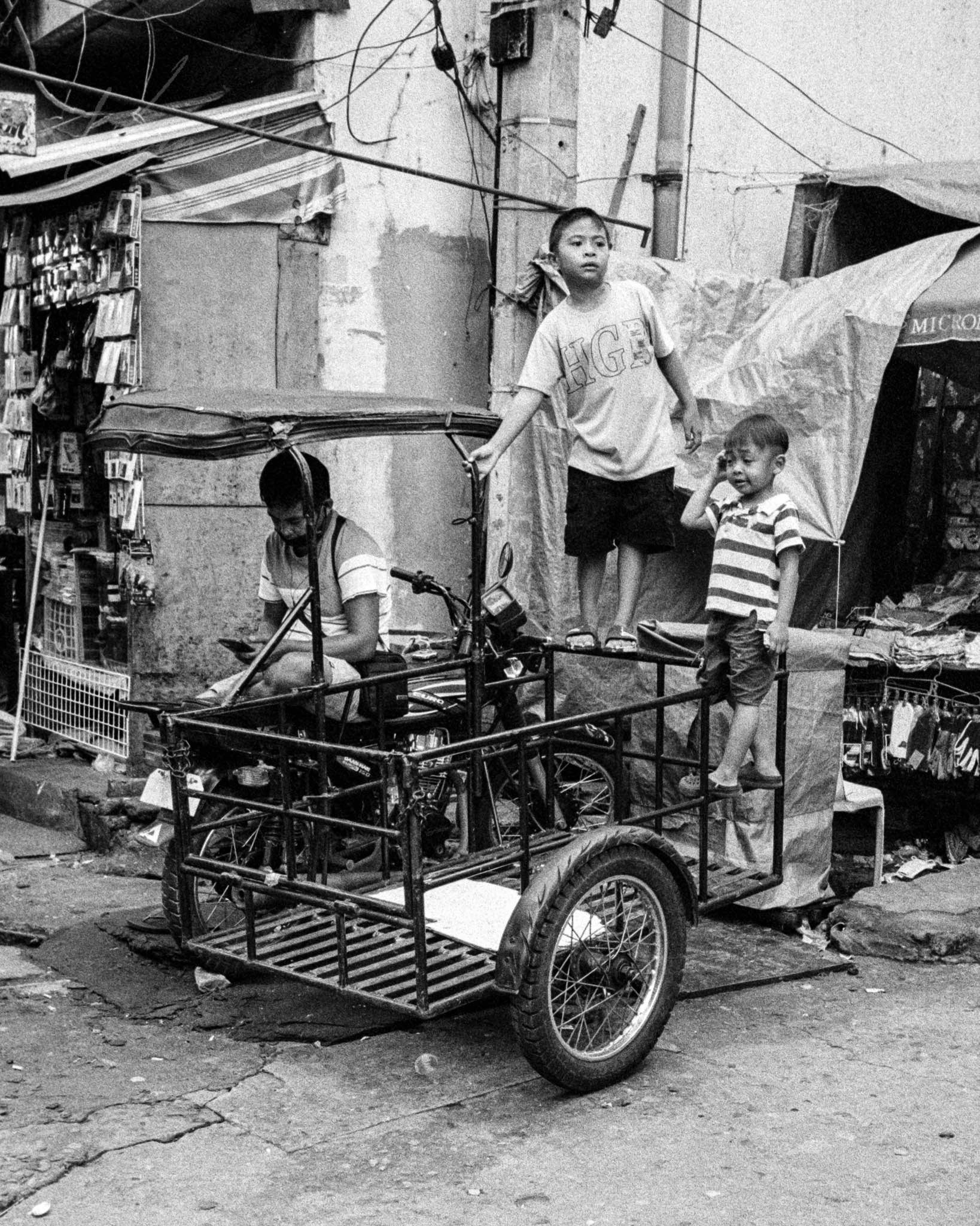Children interacting with trike in bustling, informal urban neighborhood.