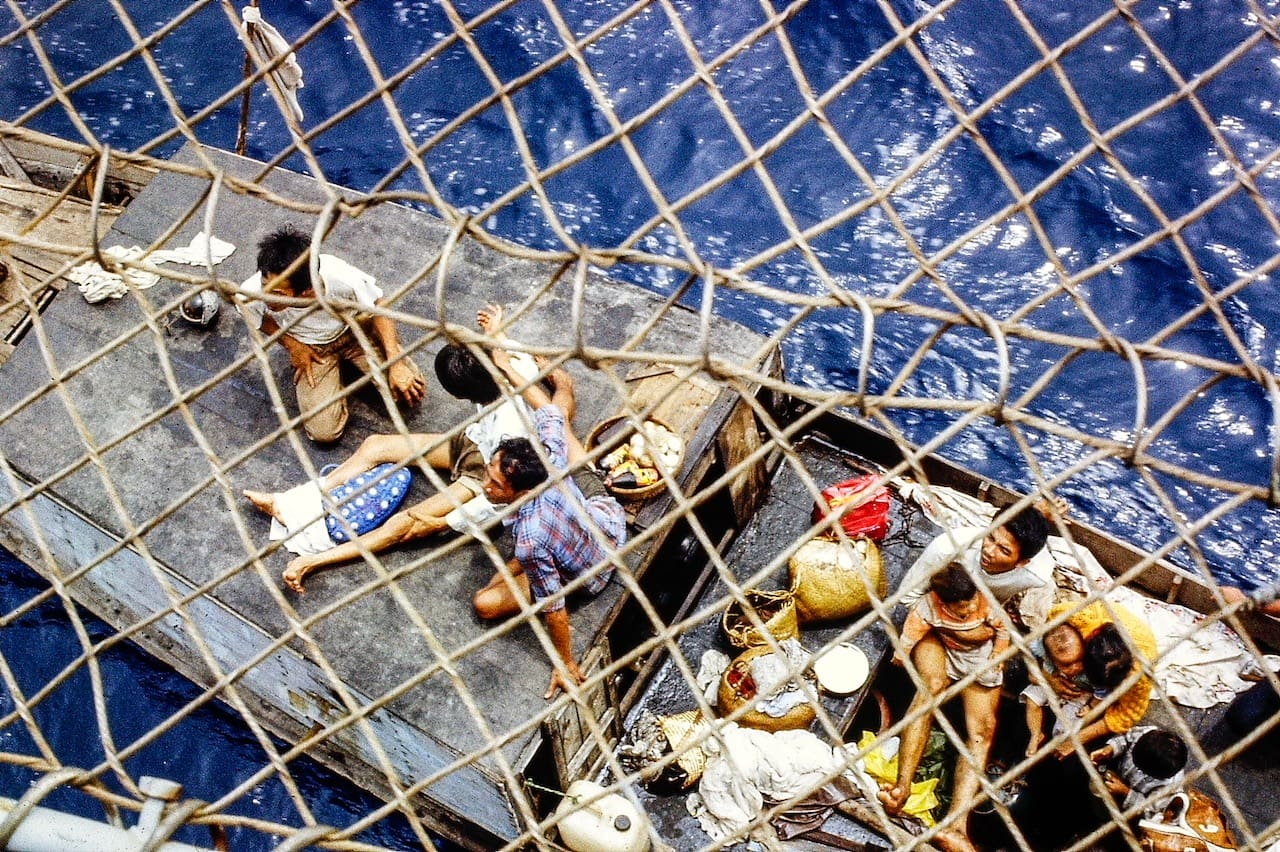 Group of Vietnamese refugees traveling on a small boat viewed from above through a netting of the USS Lockwood