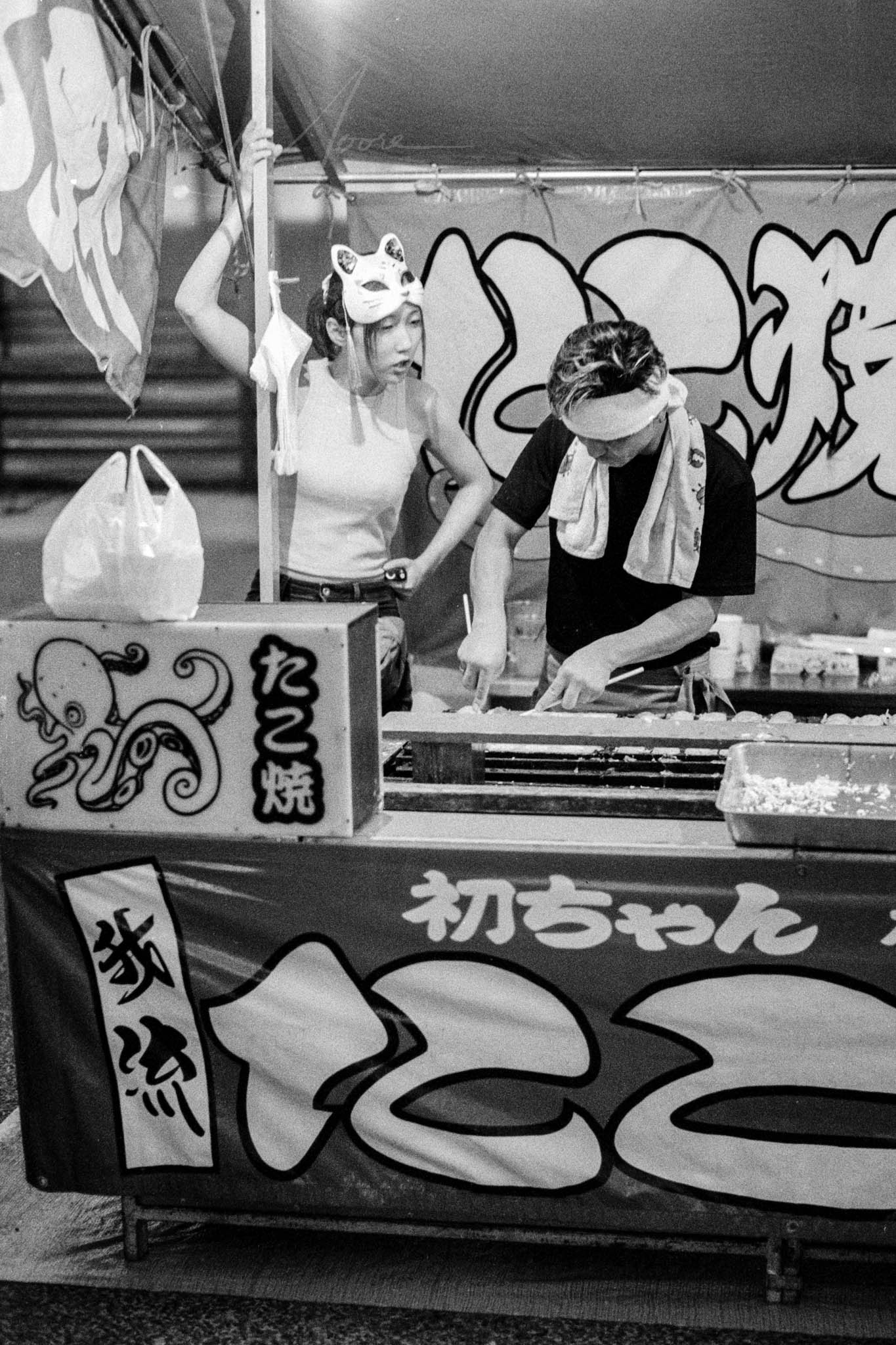 Vintage photo of Japanese festival featuring traditional fox mask and food stall.
