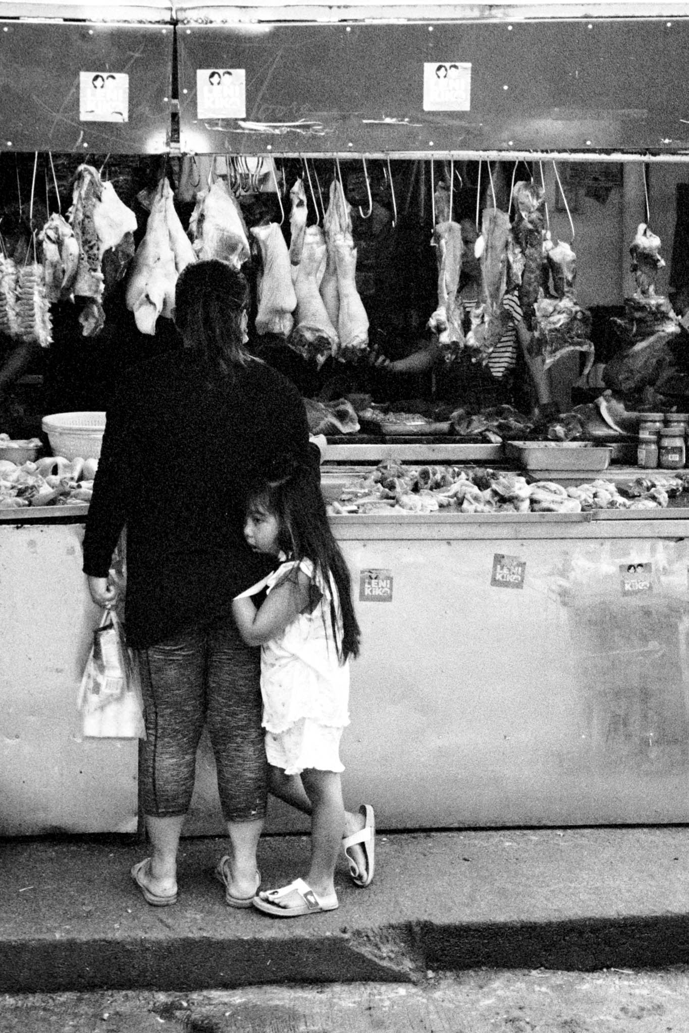Woman and child buying poultry at a traditional butcher stall in black and white photo.